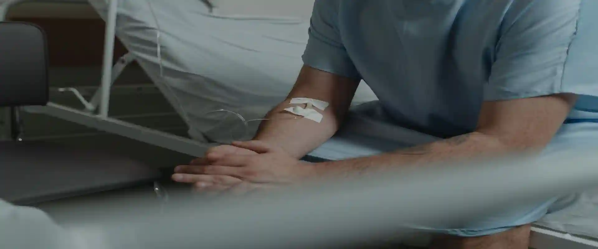 Patient in a hospital gown sitting on a bed with an IV line during colon cancer chemotherapy